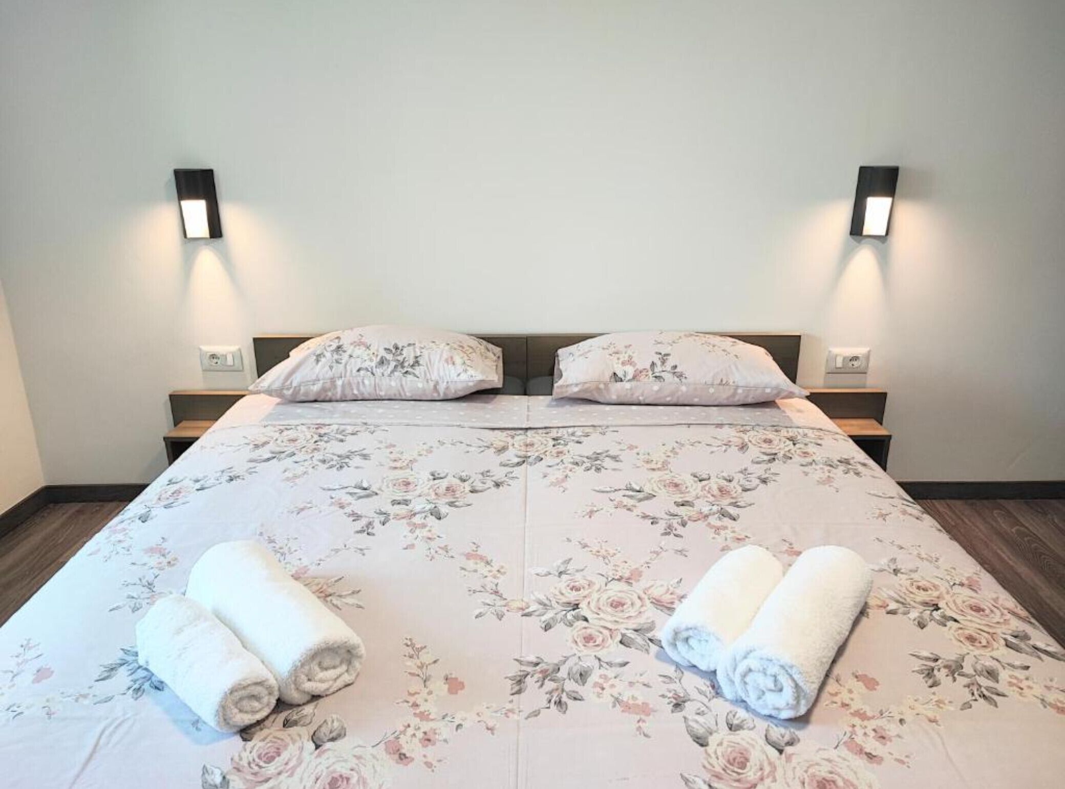 A double bed with floral bedding, two pillows, and two rolled towels.