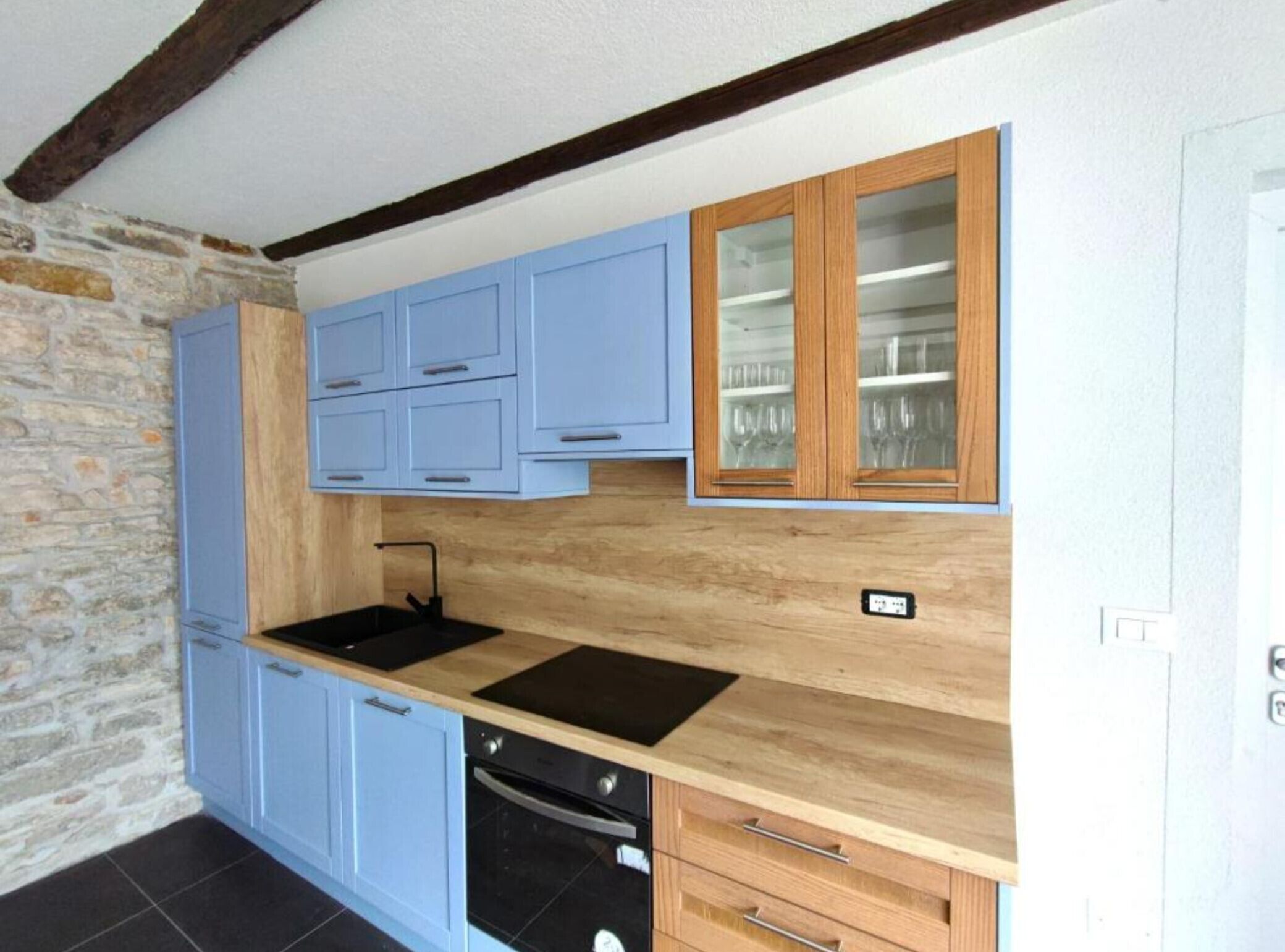 Une cuisine avec des meubles de couleur bleu clair, un plan de travail en bois et un mur en pierre.