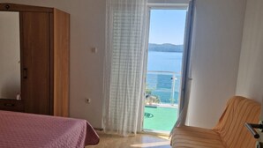 A bedroom with a bed, a wooden wardrobe, and a balcony with a view of the sea. - Apartments Bilić Trogir - Three- Bedroom Apartment With Sea View (A3) (Trogir)