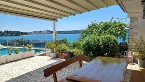 A patio with a wooden bench and table, overlooking a pool and a lake with a view of distant hills. - Apartments Bilić Trogir - Three- Bedroom Apartment With Sea View (A3) (Trogir)