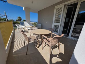 A balcony with a round table and chairs, a sliding glass door, and a view of palm trees and the sea. - M4ree Seaside Suite And Relax (Bari)