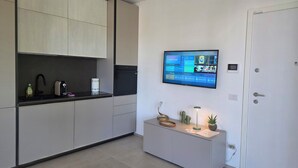 A modern kitchen with a built-in oven, a flat-screen TV mounted on the wall, and a small cabinet with decorative items. - M4ree Seaside Suite And Relax (Bari)