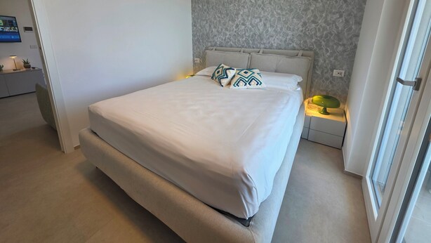 A bedroom with a bed, a nightstand, a lamp, and a television on a stand. - M4ree Seaside Suite And Relax (Bari)