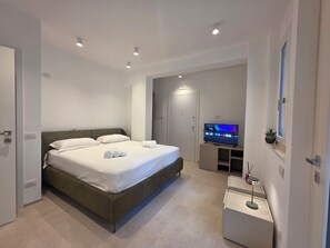 A modern hotel room with a large bed, a flat-screen TV, a small desk, and a potted plant. - M4ree Seaside Suite And Relax (Bari)