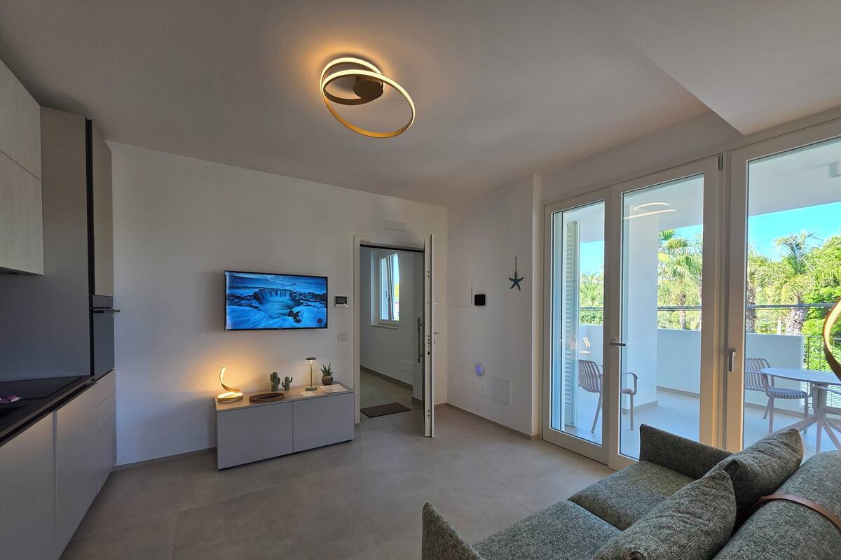 A modern living room with a flat-screen TV, a sofa, and a kitchen area with a refrigerator.