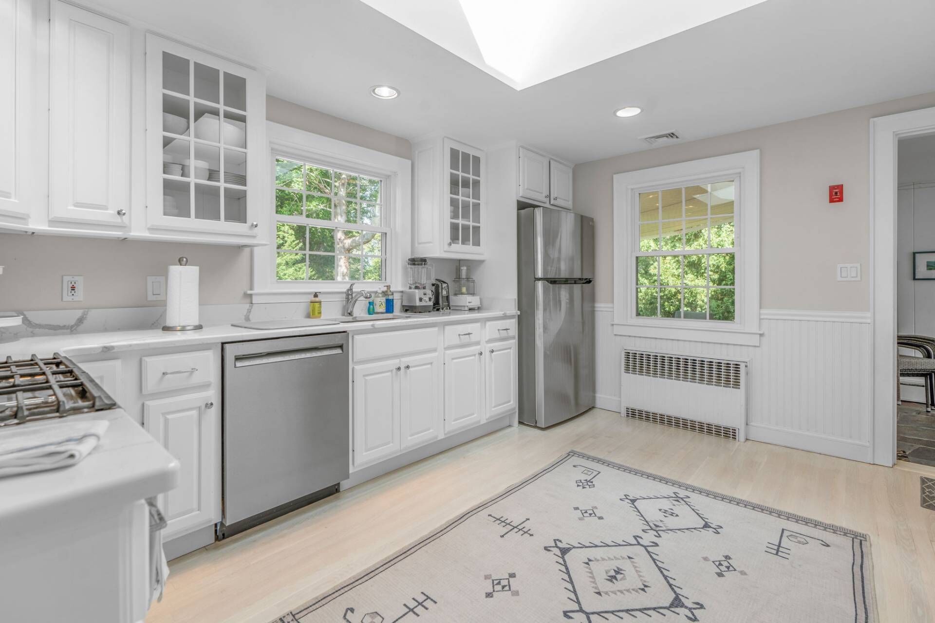 A modern kitchen with white cabinetry, a stainless steel refrigerator, and a window providing natural light.