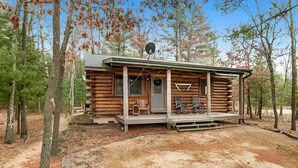 Une cabane en rondins avec un porche, une antenne parabolique et un banc.