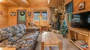 L’intérieur chaleureux d’un chalet avec un canapé, une table en bois, une cheminée en pierre et un téléviseur.