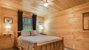 Une chambre à coucher aux murs lambrissés, avec un lit, deux lampes de chevet, un ventilateur de plafond et des tableaux encadrés.