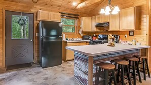 Une cuisine moderne avec des meubles en bois, un réfrigérateur noir, un grand îlot central avec des tabourets et un sol en pierre.