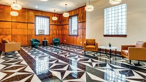 Een ruime lobby met een vloer met een geometrisch patroon, houten paneelbekleding en meerdere zithoeken met moderne stoelen en een klein tafeltje.