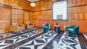 Een hal met houten lambrisering, een zwart-wit geometrisch betegelde vloer en twee smaragdgroene fauteuils.