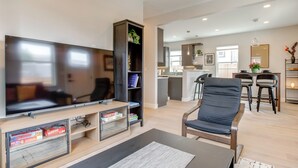 Een moderne woonkamer met een flatscreen-televisie, een boekenkast en een eethoek, met een keuken op de achtergrond.