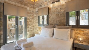Een slaapkamer met stenen muren, een groot bed met witte lakens en uitzicht op het omliggende landschap.