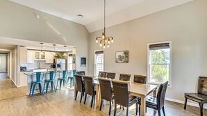 Un'ampia sala da pranzo con tavolo e sedie in legno, una cucina sullo sfondo e ampie finestre che lasciano entrare la luce naturale.