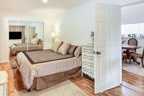 Un dormitorio con cama, cómoda, espejo y puerta que da a un comedor.