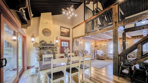 A spacious living room with a wooden dining table and chairs, a staircase, and a cozy fireplace. - Willow Brook Getaway: Hot Tub, Deck in Mifflinburg (Mifflinburg)
