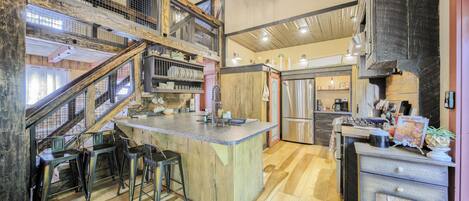 Una cocina amplia con una isla central, pisos de madera y un entresuelo con escalera.