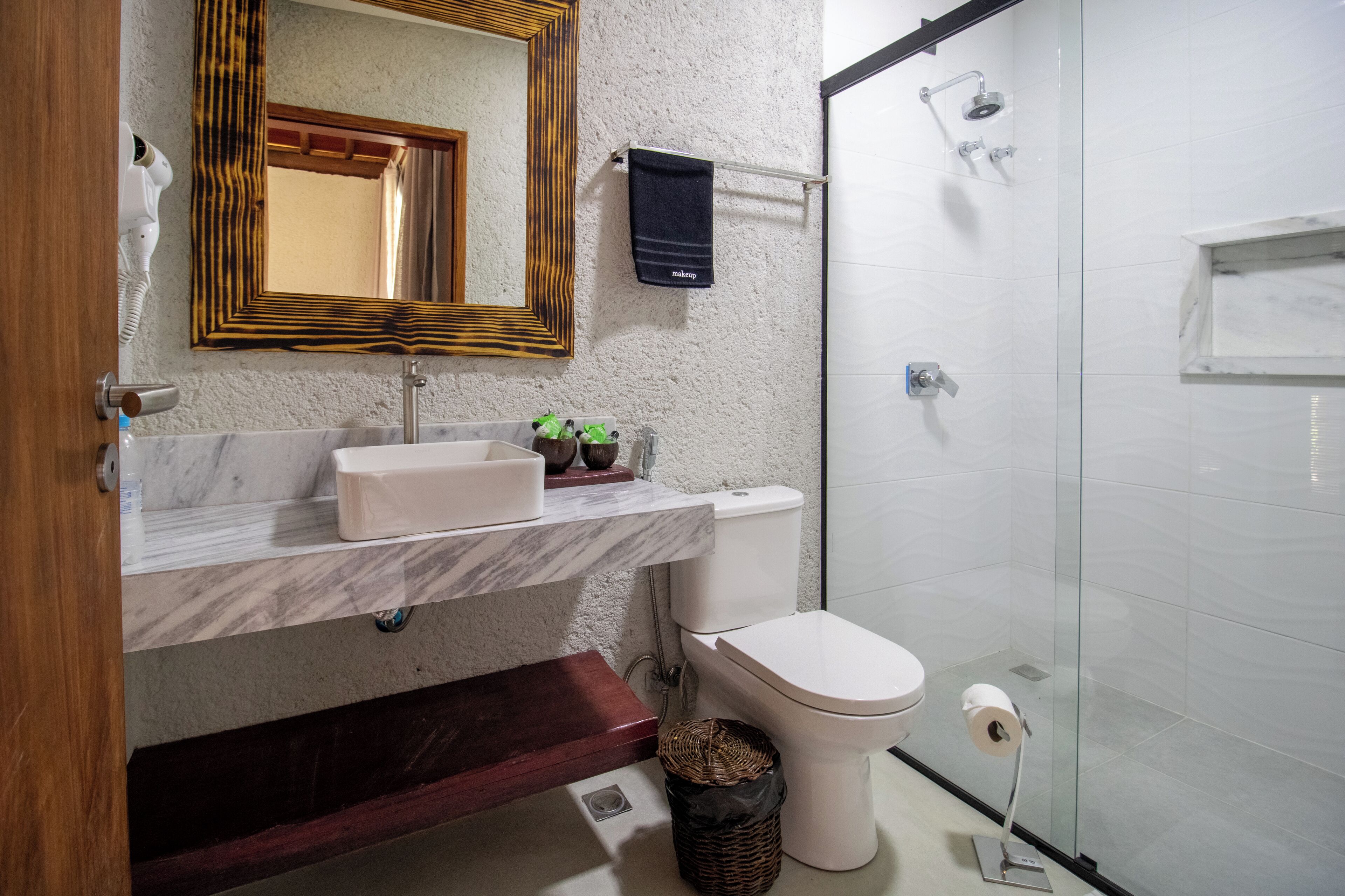 A bathroom with a marble sink, a toilet, a shower, and a mirror with a wooden frame.