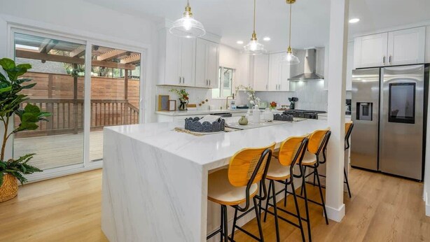 A modern kitchen with white cabinets, a central island with bar stools, stainless steel appliances, and pendant lighting.