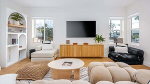 A spacious living room with a large flat-screen TV mounted on the wall, a wooden console table, and two sofas.