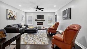 Un salon moderne avec un canapé en cuir noir, un fauteuil en cuir marron, un tapis à motifs de marbre et un ventilateur de plafond.