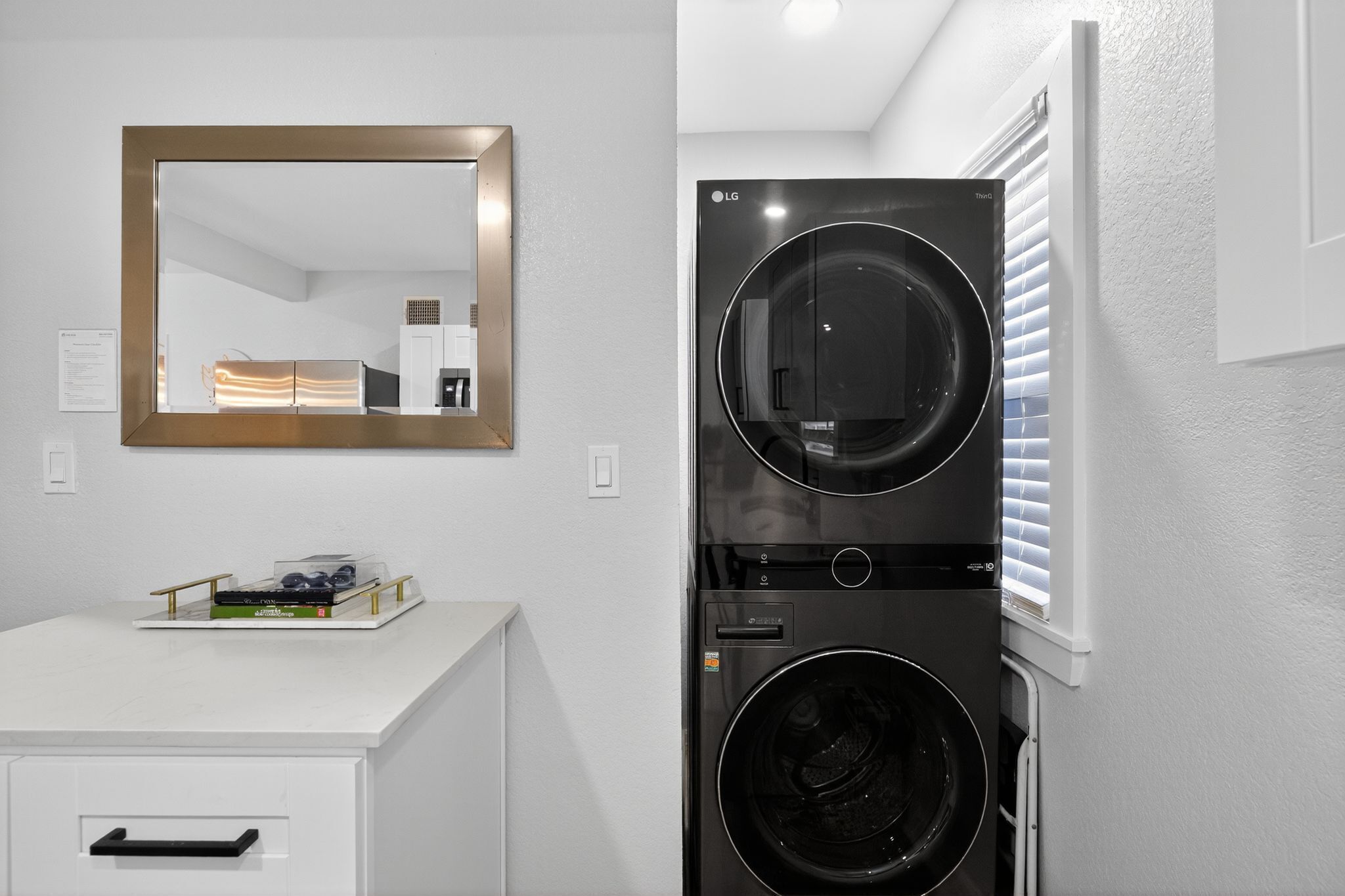 A laundry room with a double washer and dryer, a white sink with a mirror above it, and a small cabinet below.