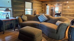 Un intérieur chaleureux de chalet en bois, avec un canapé d’angle, un pouf, un plancher en bois et une lampe au style rustique.