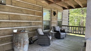 Une cabane en rondins dotée d’un porche aménagé avec des meubles en osier, une lanterne et présentant un style rustique.