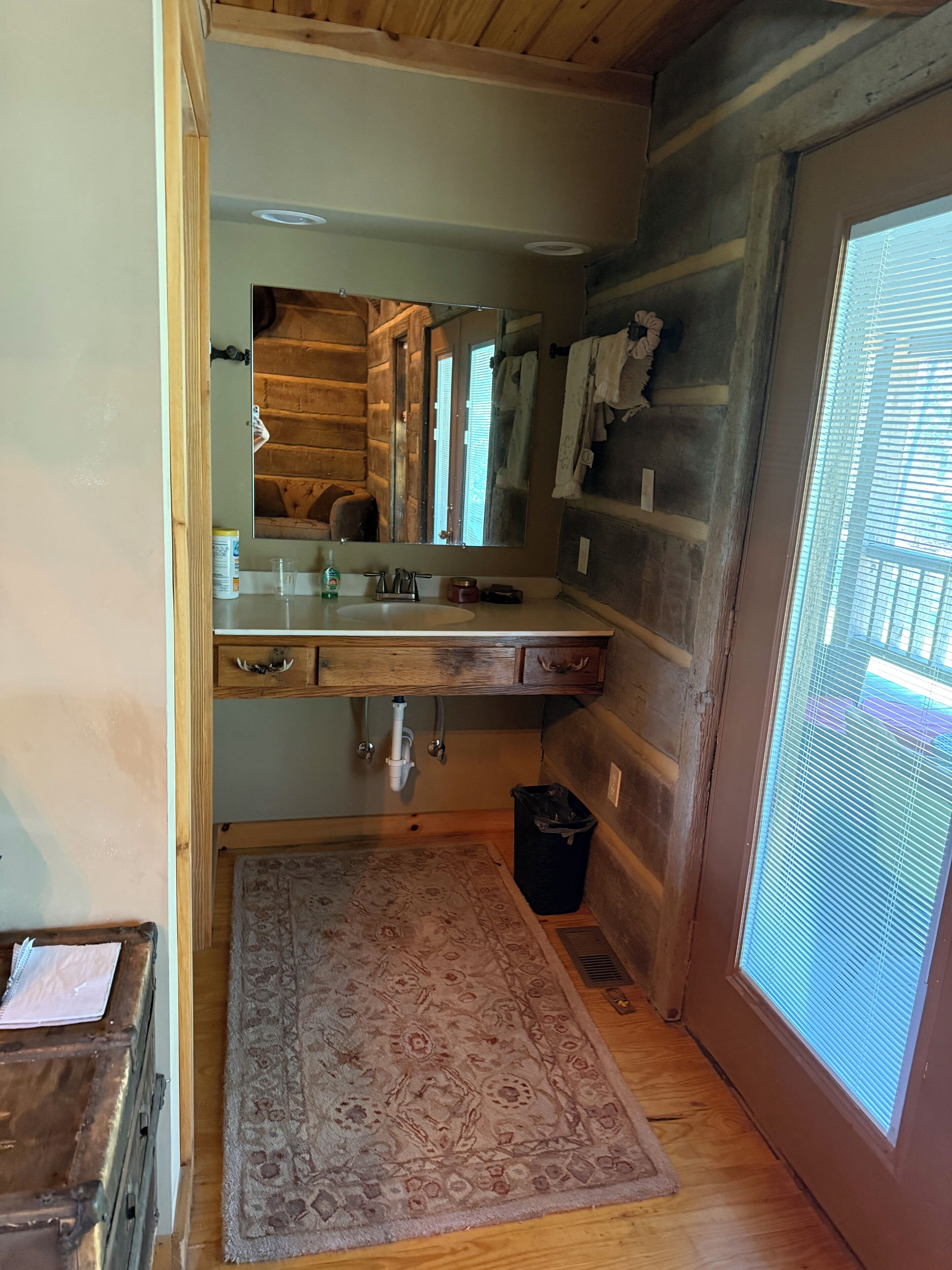 A bathroom with a wooden vanity, a large mirror, a sink, and a window with blinds.