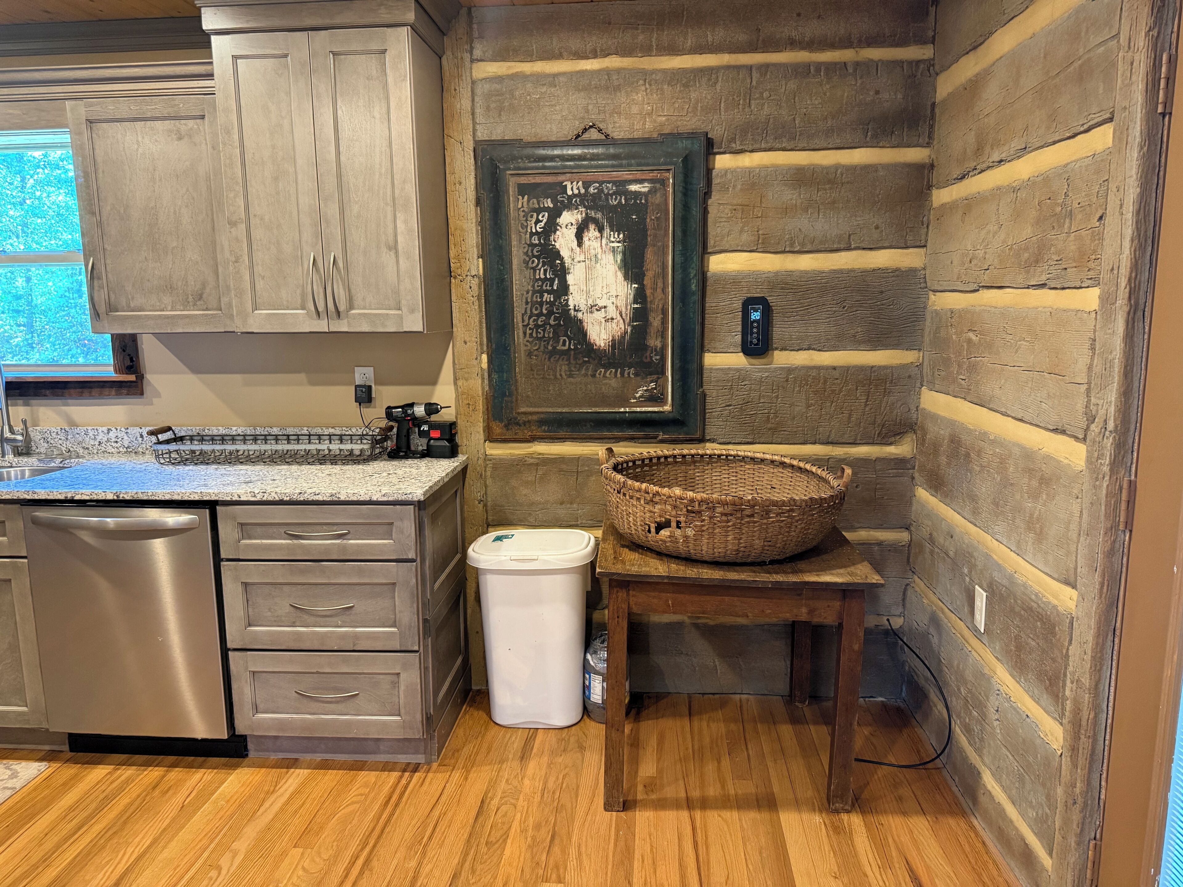 A kitchen with wooden cabinets, a granite countertop, a stainless steel dishwasher, a white trash bin, and a woven basket on a wooden table.