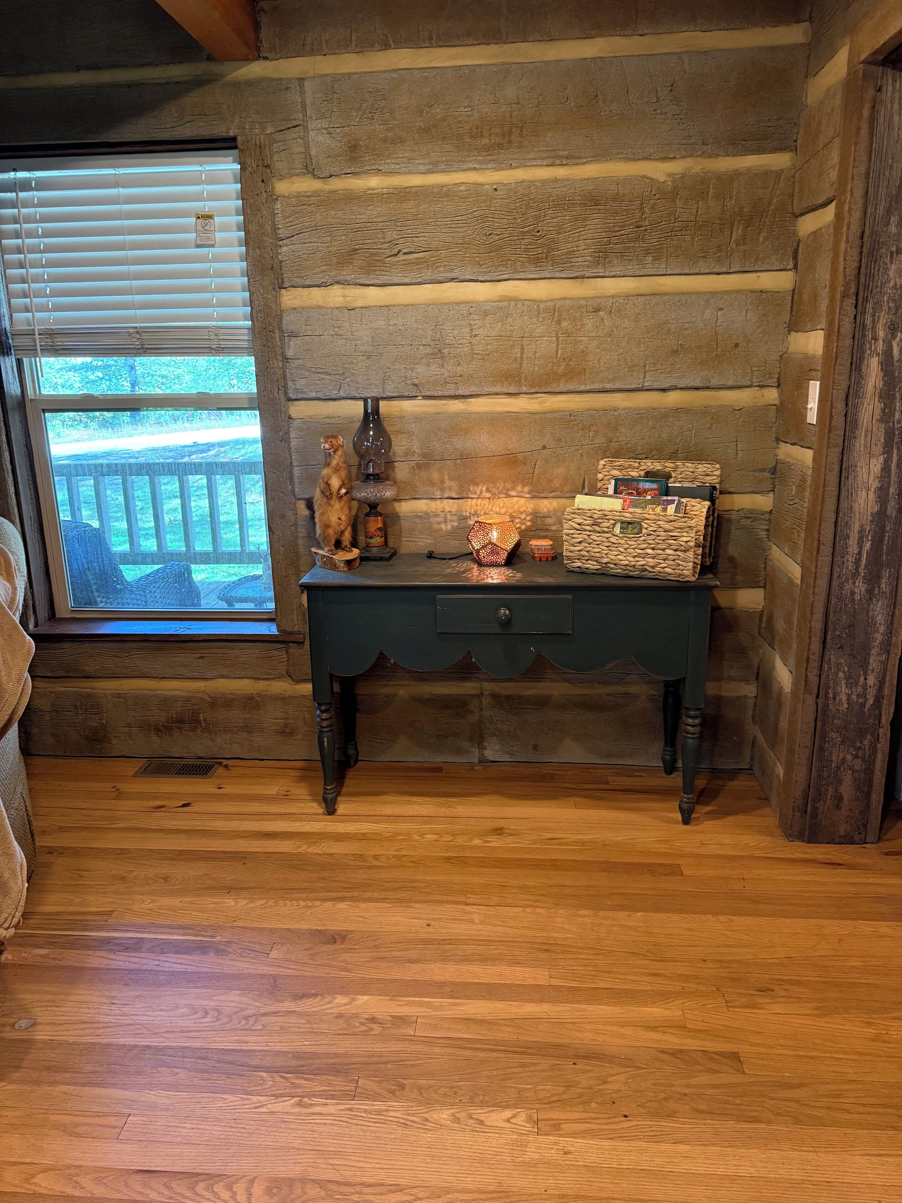 A rustic wooden room with a wooden bench, a small table with decorative items, and a window with blinds.