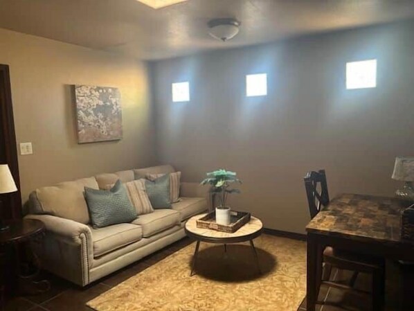 A living room with a beige sofa, a small round table with a plant, and a dining table with chairs.
