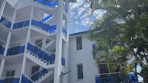 A multi-story building with white exterior walls and blue railings. - Charming 1-bedroom studio facing the pool, in the heart of Sosua (Sosúa)