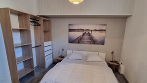 Een slaapkamer met een groot bed, houten planken, een nachtkastje en een hanglamp.