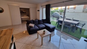 Een moderne woonkamer met een donkere bank, een kleine tafel met een plant en een glazen schuifdeur die leidt naar een terras.
