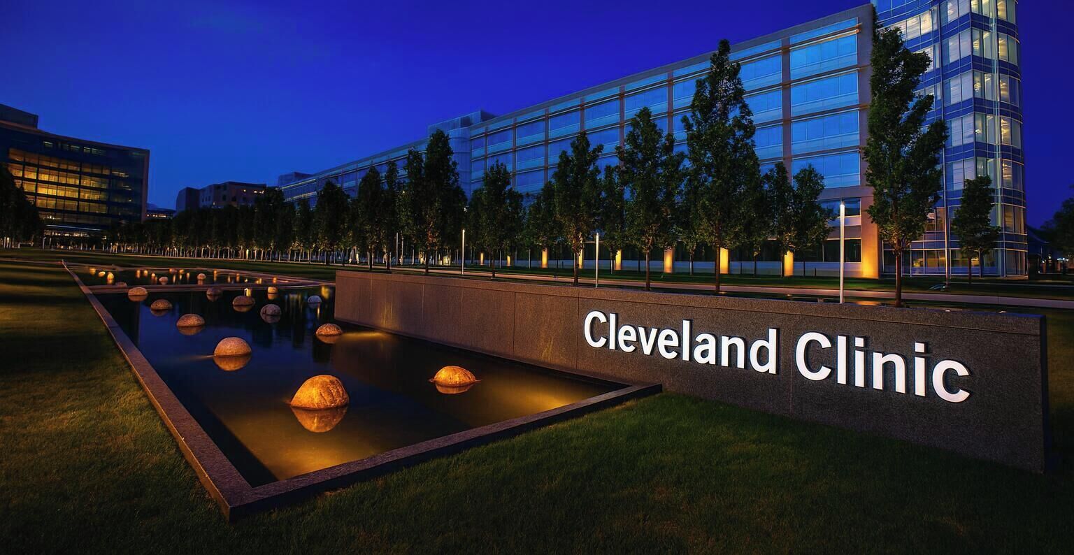 A modern building with a sign reading "Cleveland Clinic" and a landscaped area with a water feature.