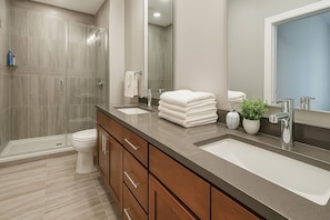 Un baño moderno con ducha de vidrio, inodoro, lavamanos con espejo y una planta en maceta.