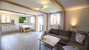 A cozy living room with a wooden coffee table, a sofa, and a dining area with a table and chairs. - Koppelkuck vacation apartment on a beautiful vacation farm with pool and sauna Ostseena (Schwartbuck)