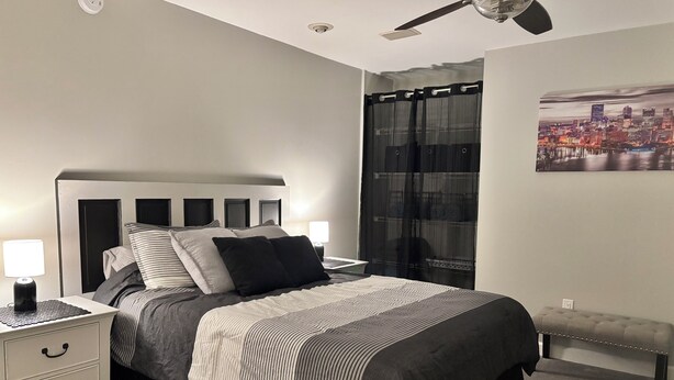 A bedroom with a bed, nightstands, a bench, a ceiling fan, and a cityscape painting on the wall. - Cozy, spacious 1 bdrm apt in Bloomfield with off street parking. Great location! (Pittsburgh)