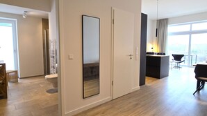 Un apartament modern amb un terra de fusta, un gran mirall, zona de menjador amb taula i cadires, i vistes a través d'una finestra gran.
