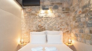 Una cama con ropa blanca y toallas, una pared de piedra y dos luces fijadas a la pared.