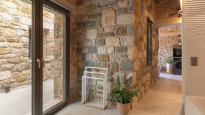 Un pasillo con paredes de piedra, una puerta de vidrio corredera, estructura de metal y una planta en maceta.