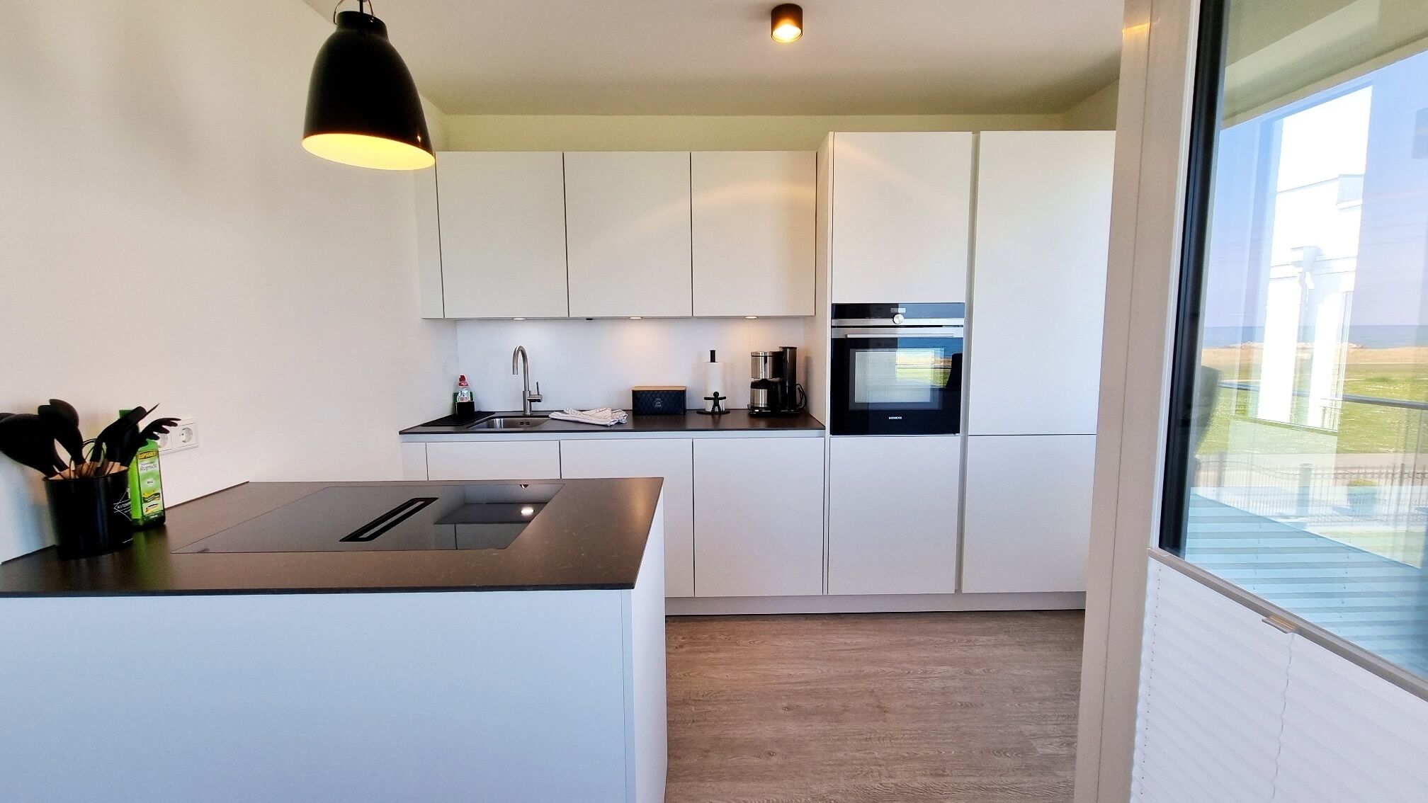 A modern kitchen with white cabinets, a stainless steel sink, and a built-in oven.