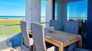 A balcony with wicker chairs and a wooden table, overlooking a beach and ocean. - Baltic Sea vacation apartment Surfside - sea view from every window (Schönberg (Holstein))