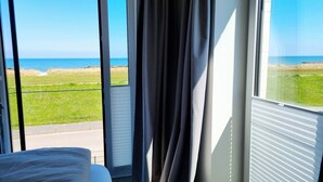 A room with a large window overlooking a beach and grassy area. - Baltic Sea vacation apartment Surfside - sea view from every window (Schönberg (Holstein))