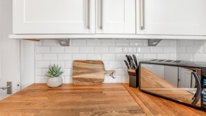 A kitchen with white cabinets, a wooden cutting board, a potted plant, and a microwave.