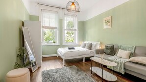 A modern living room with a bed, sofa, and coffee table, large windows, and a hanging light fixture.
