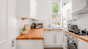 A modern kitchen with white cabinetry, a wooden countertop, a built-in oven, and a window providing natural light.