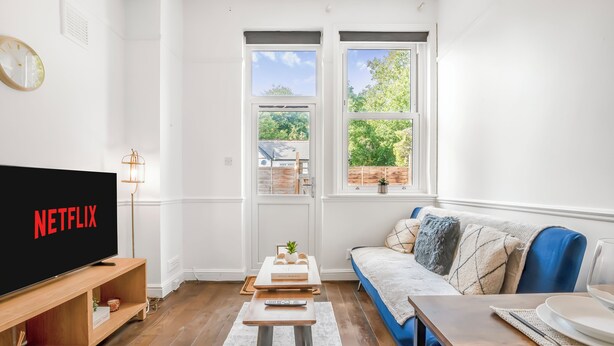 A living room with a TV displaying 'NETFLIX', a wooden coffee table, a blue sofa, and a view of a garden through a window.